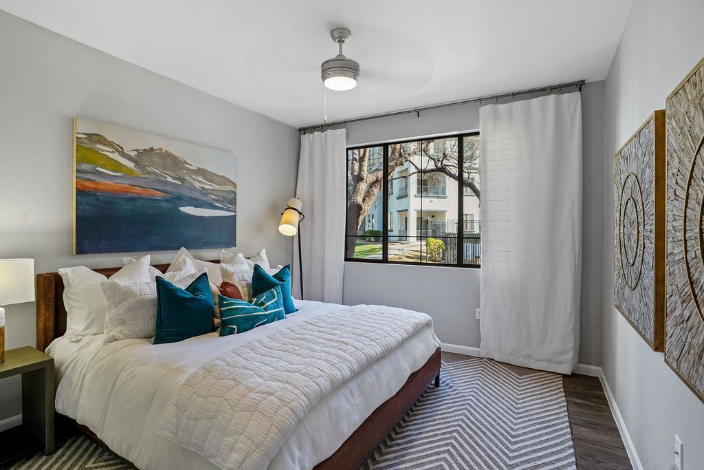 Bedroom in a modern apartment with a king-size bed, decorative pillows, a window view, and wall art.