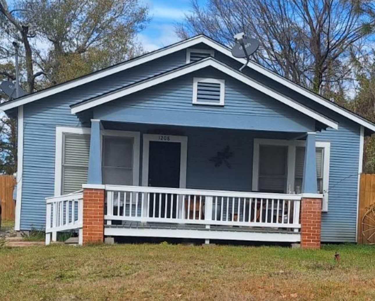 Blue house with white porch and brick columns, sitting on a grassy yard.