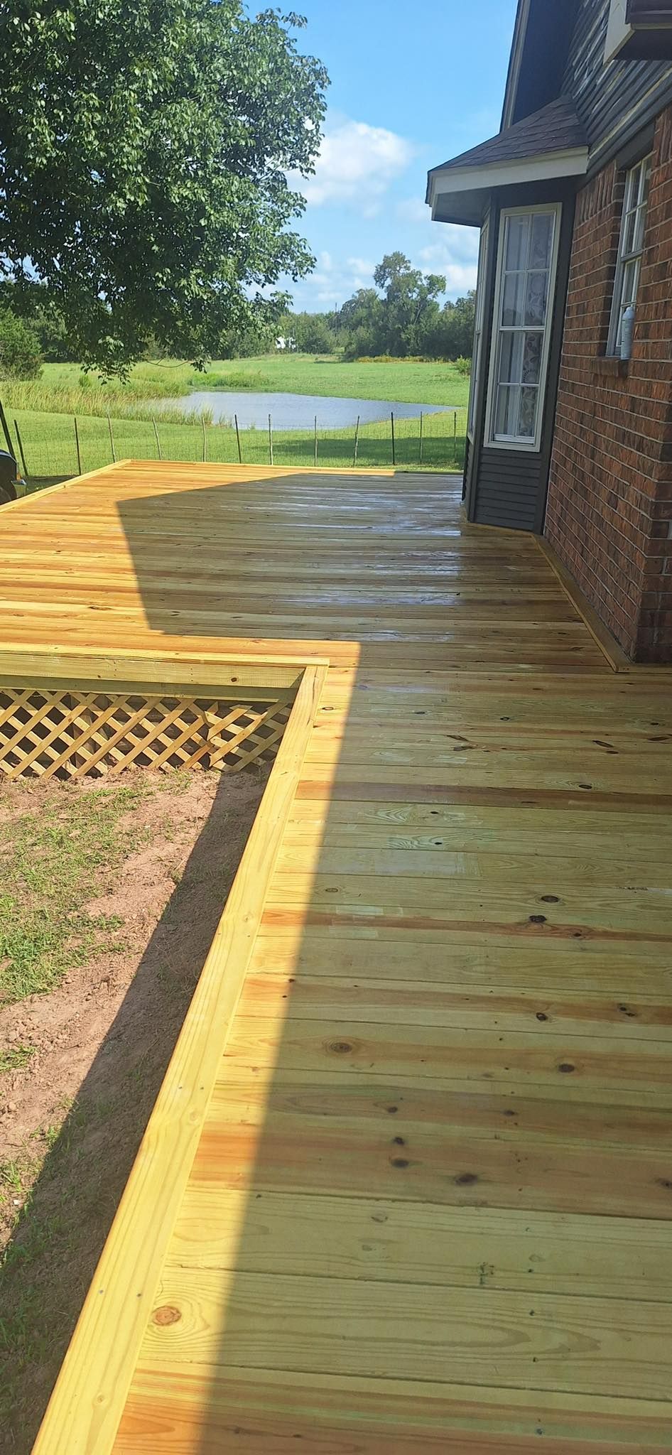 Wooden deck beside a brick building, leading toward a yard and water.