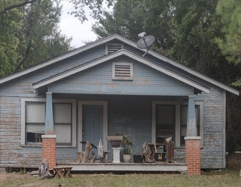 Blue, weathered house with porch, satellite dish, and red brick pillars.