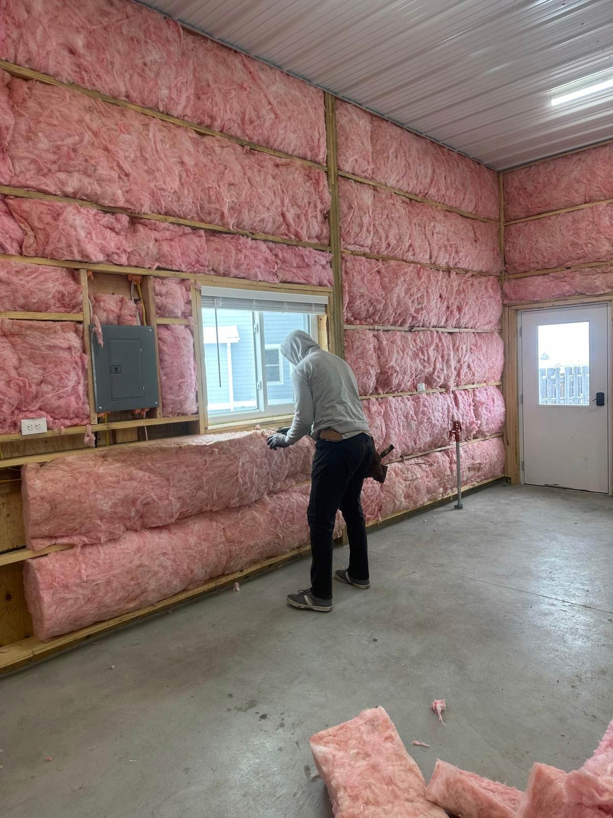 Man installing pink fiberglass insulation in a building, around a window.