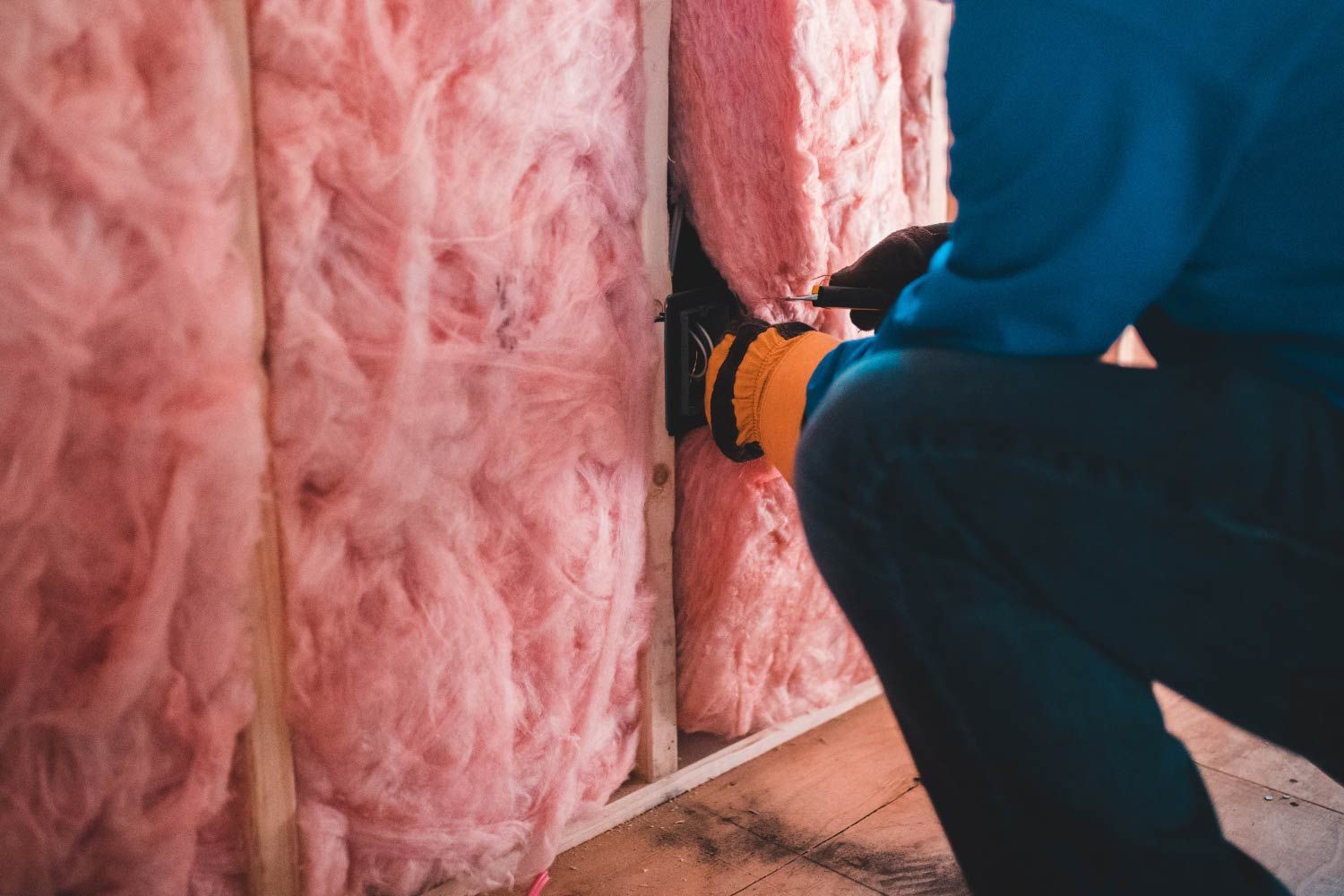 A man adding fiberglass insulation to the wall