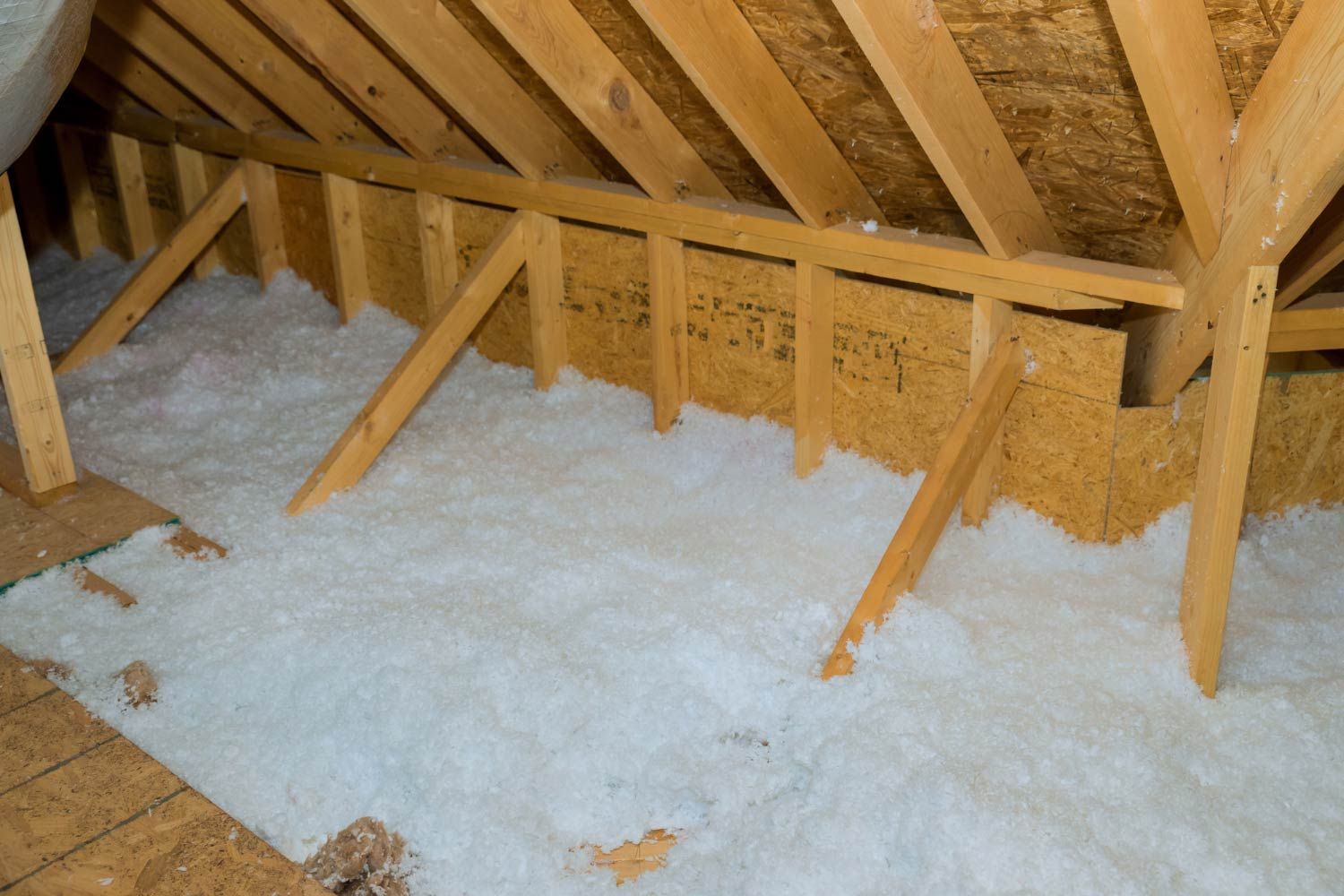 Attic interior with wooden beams and white insulation covering the floor.