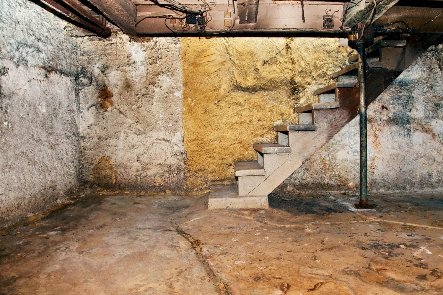 Basement with concrete stairs, walls showing wear, and support beams.