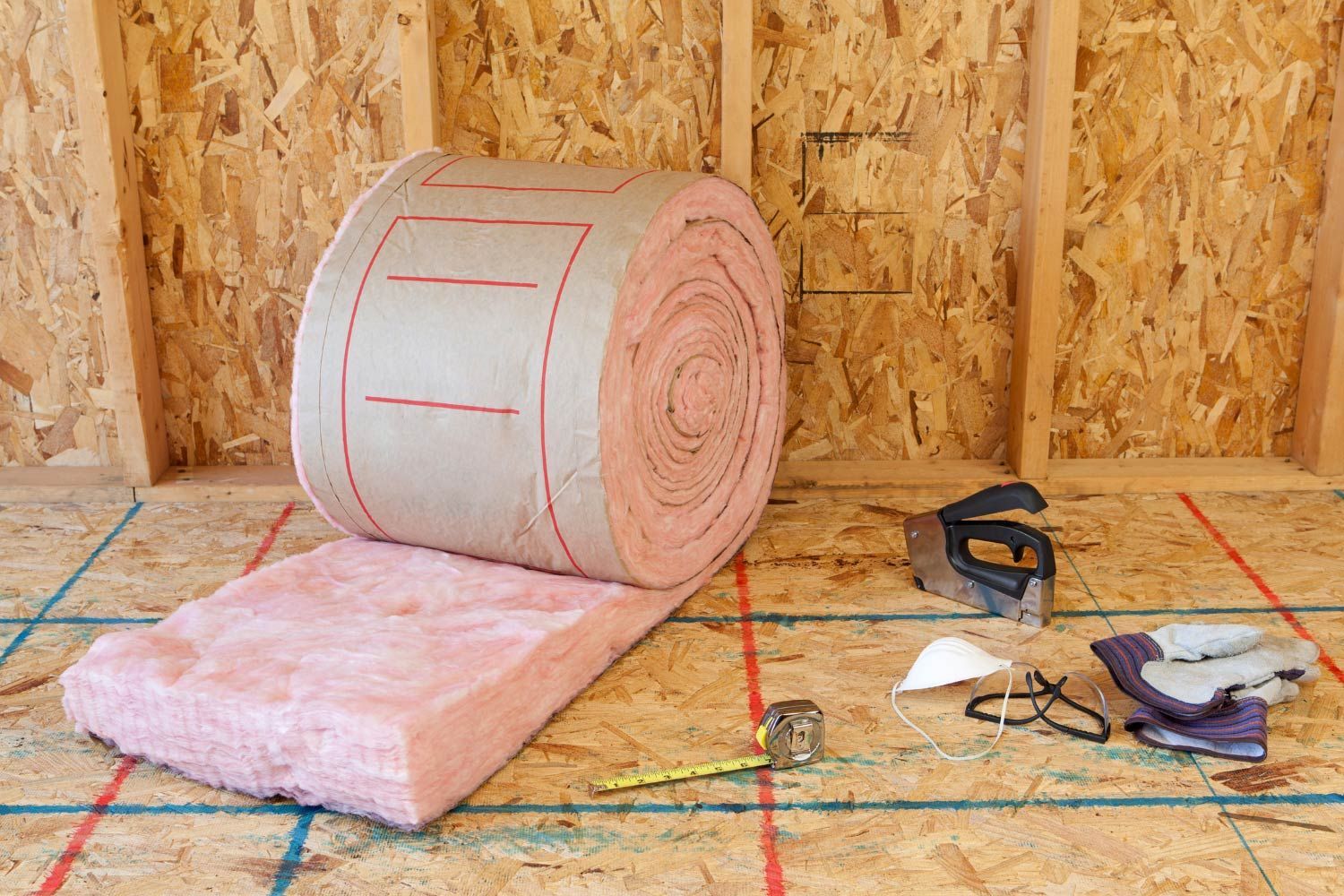 Worker spraying insulation into wall studs. Beige protective suit, hose, interior setting.
