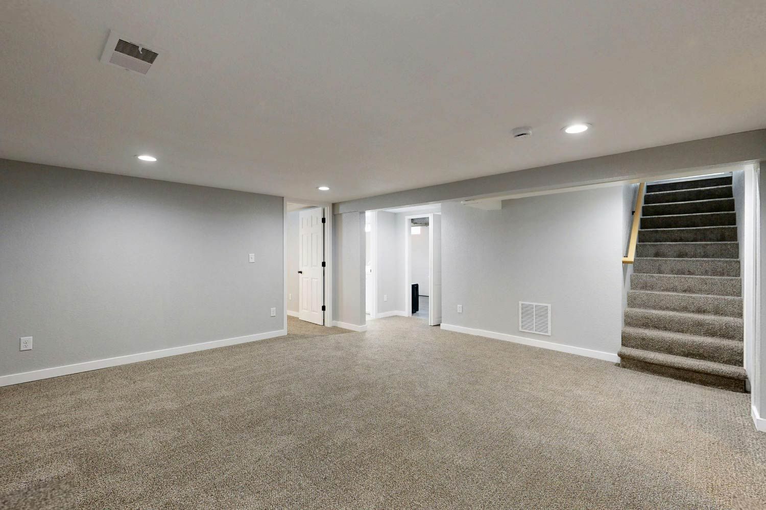 Empty basement with gray walls, beige carpet, and a staircase.