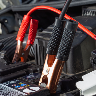 Battery charger clamps attached to a car battery inside an engine compartment