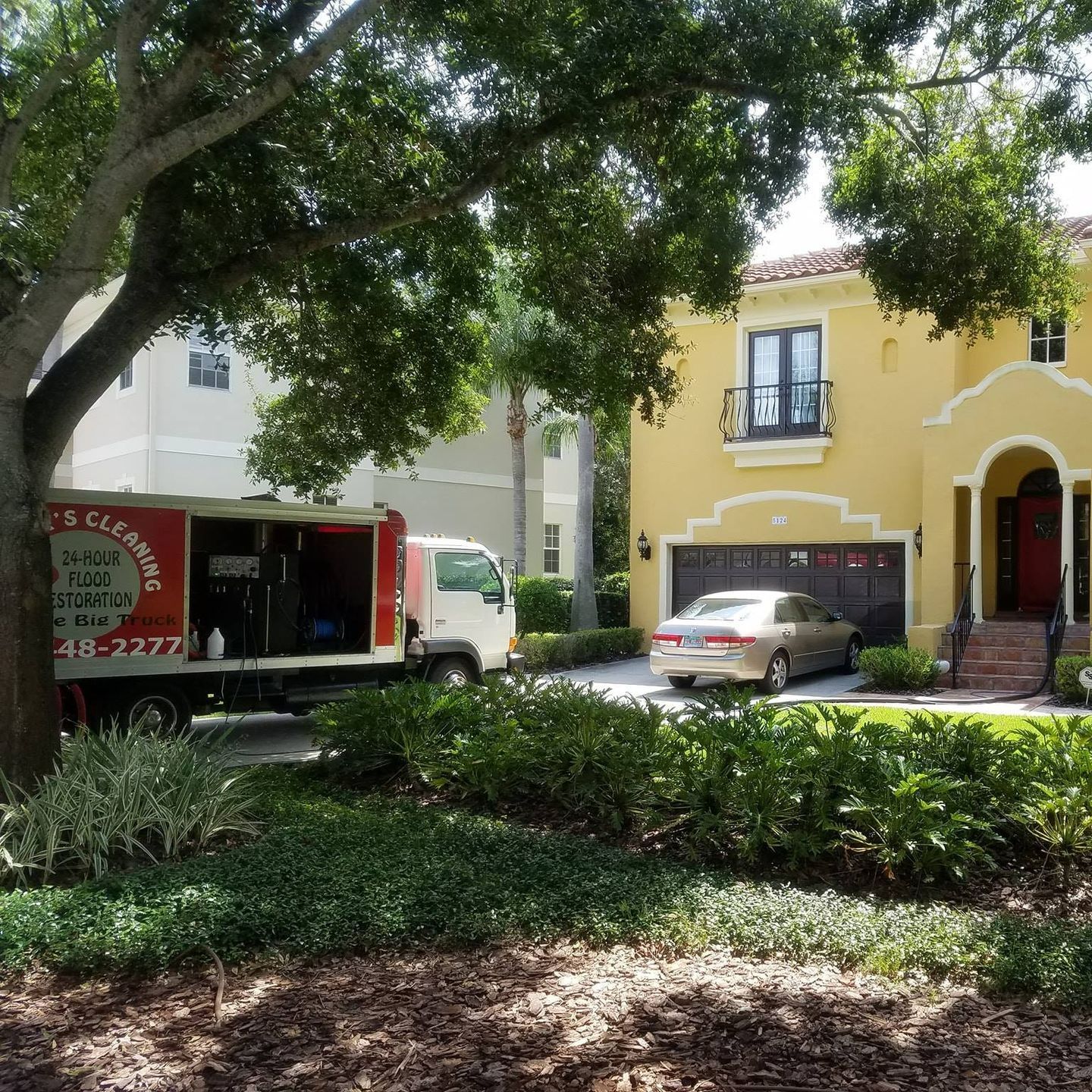 A cleaning truck is parked in front of a yellow house