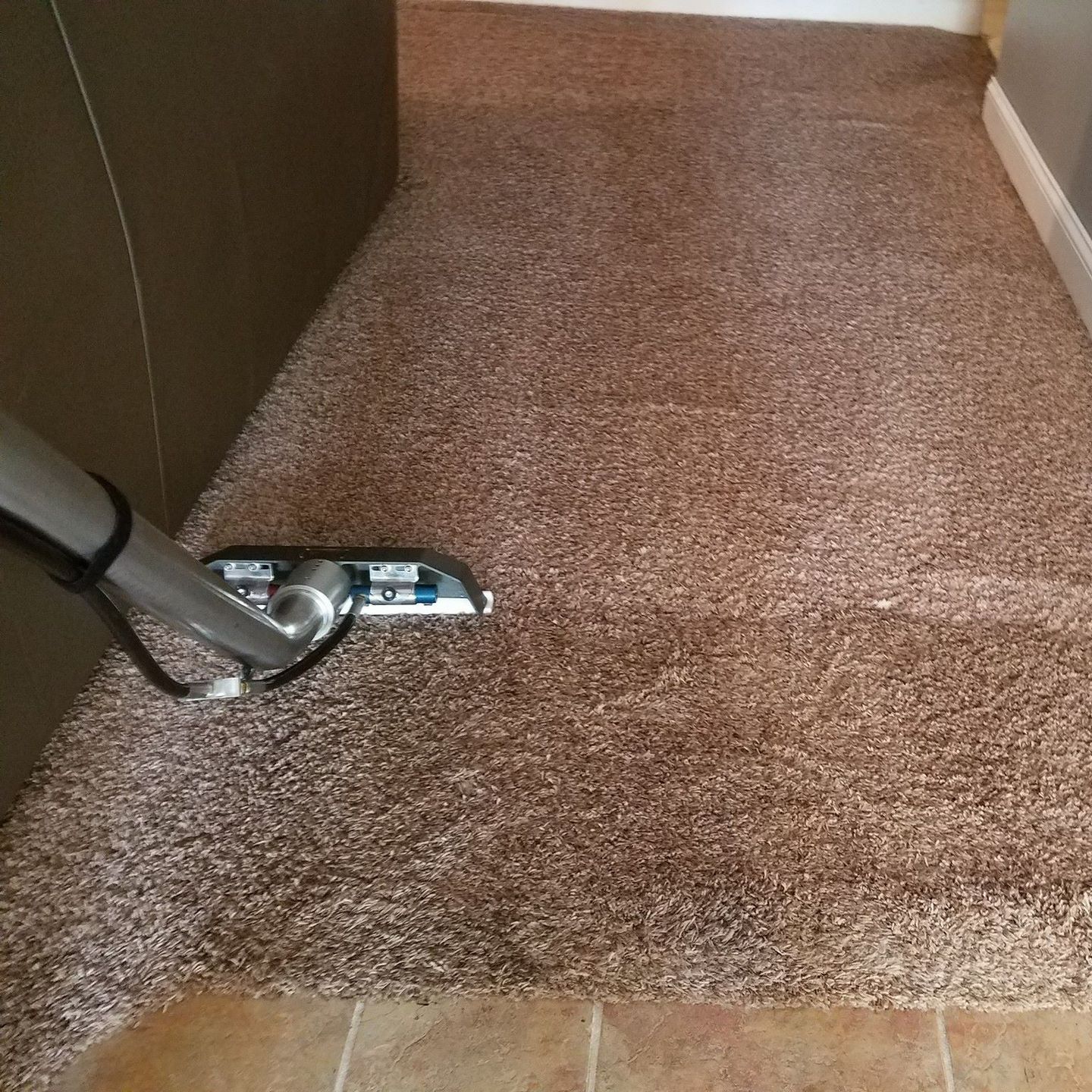 A vacuum cleaner is being used to clean a brown carpet
