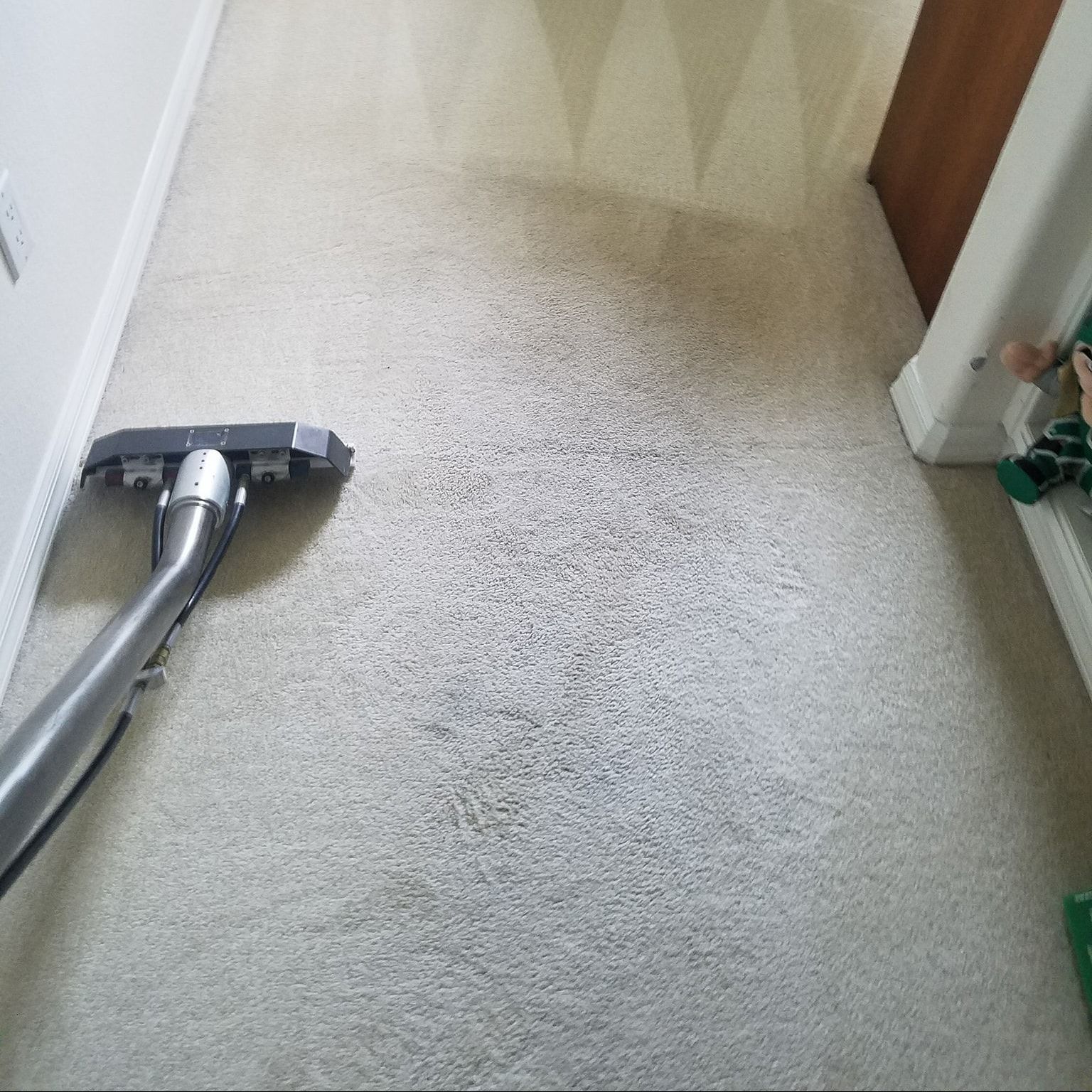 A vacuum cleaner is cleaning a carpet in a hallway.