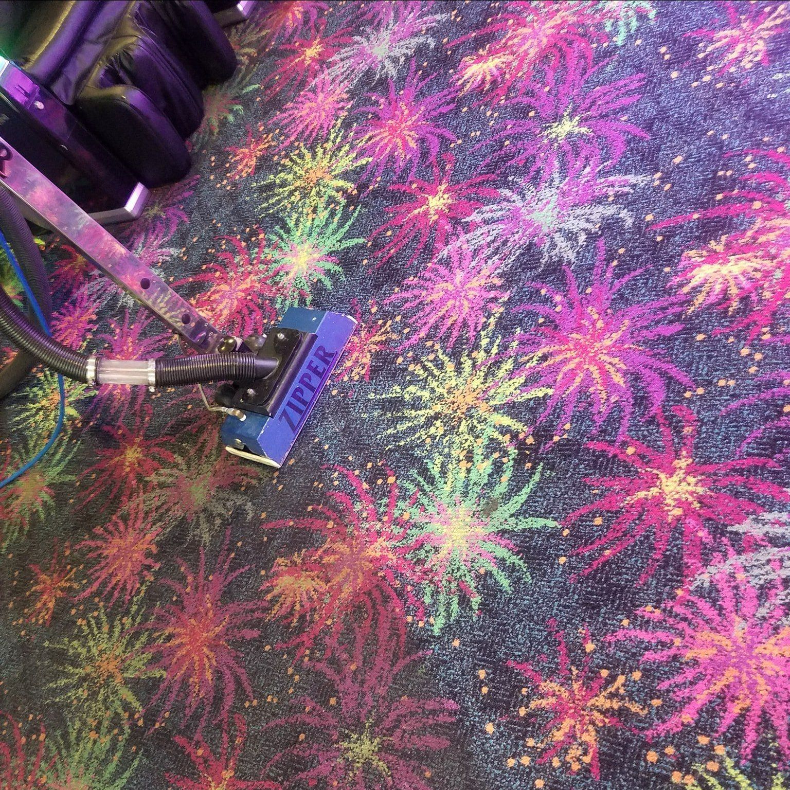 A vacuum cleaner is cleaning a colorful carpet with fireworks on it.