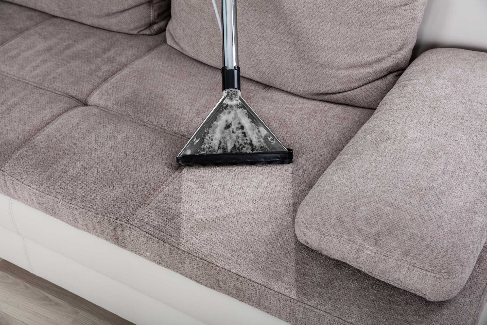 A vacuum cleaner is cleaning a couch in a living room.
