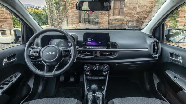 Interior view of a Kia car dashboard: black and gray console, steering wheel, infotainment screen, and gear shift.