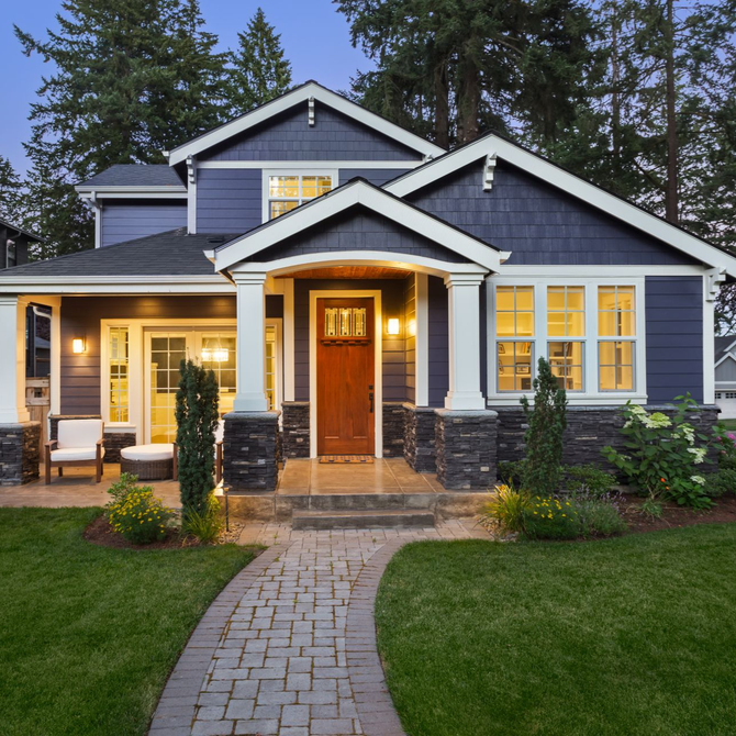 Blue house with white trim, lit porch, stone walkway, and manicured front lawn at dusk
