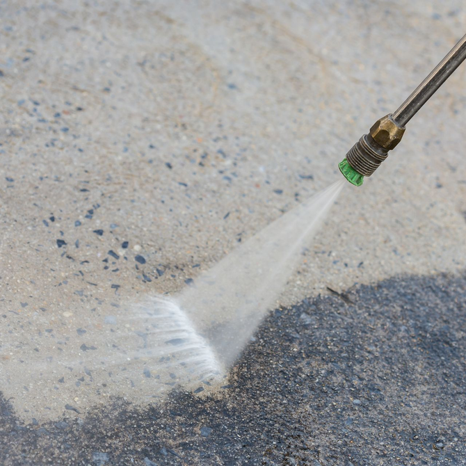 Pressure washing concrete with a spray nozzle, blasting away dirt on a textured surface