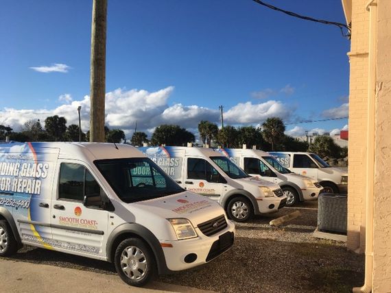 White service vans with logos parked in a row, under a bright blue sky. The vans are likely for glass repair. White service vans with logos parked in a row, under a bright blue sky. The vans are likely for glass repair.