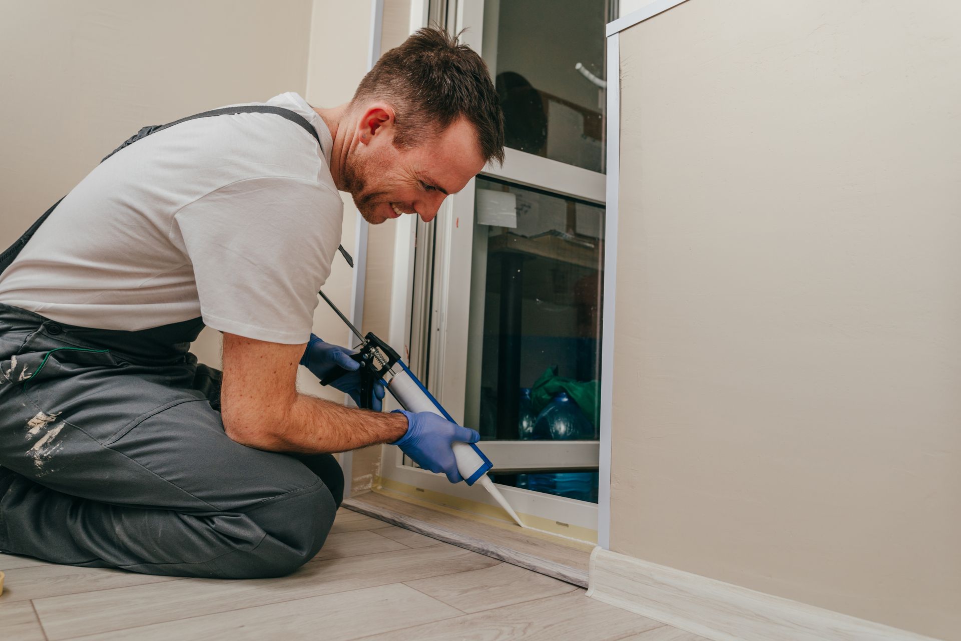 A contractor wearing overalls sealing a door.