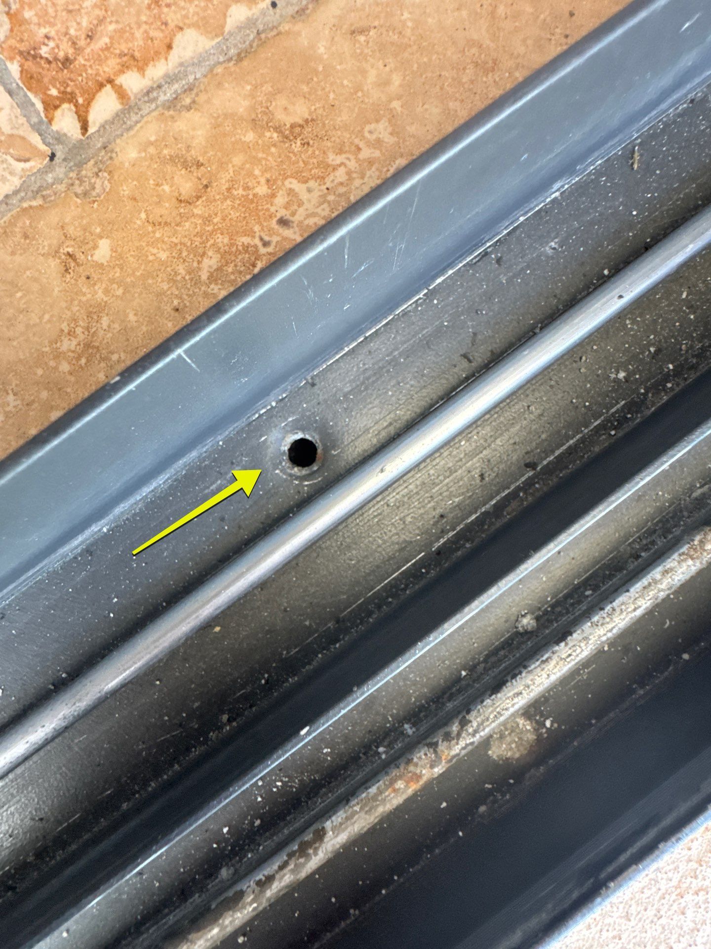 A yellow arrow points to a small drainage hole in the metal track of a sliding glass door.