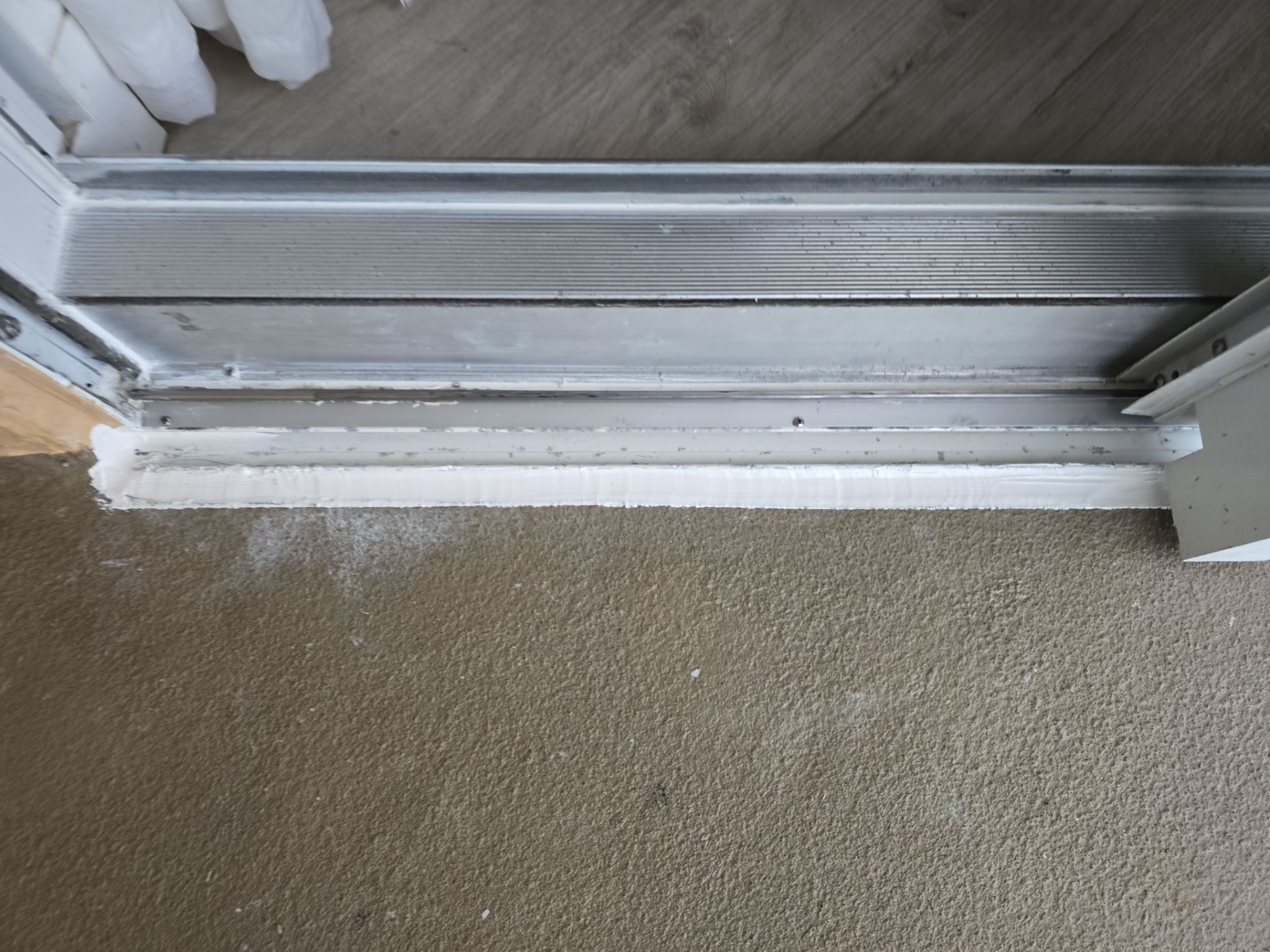 A sliding door threshold showing a gap between the metal frame and the concrete floor, sealed with a bead of white caulk.