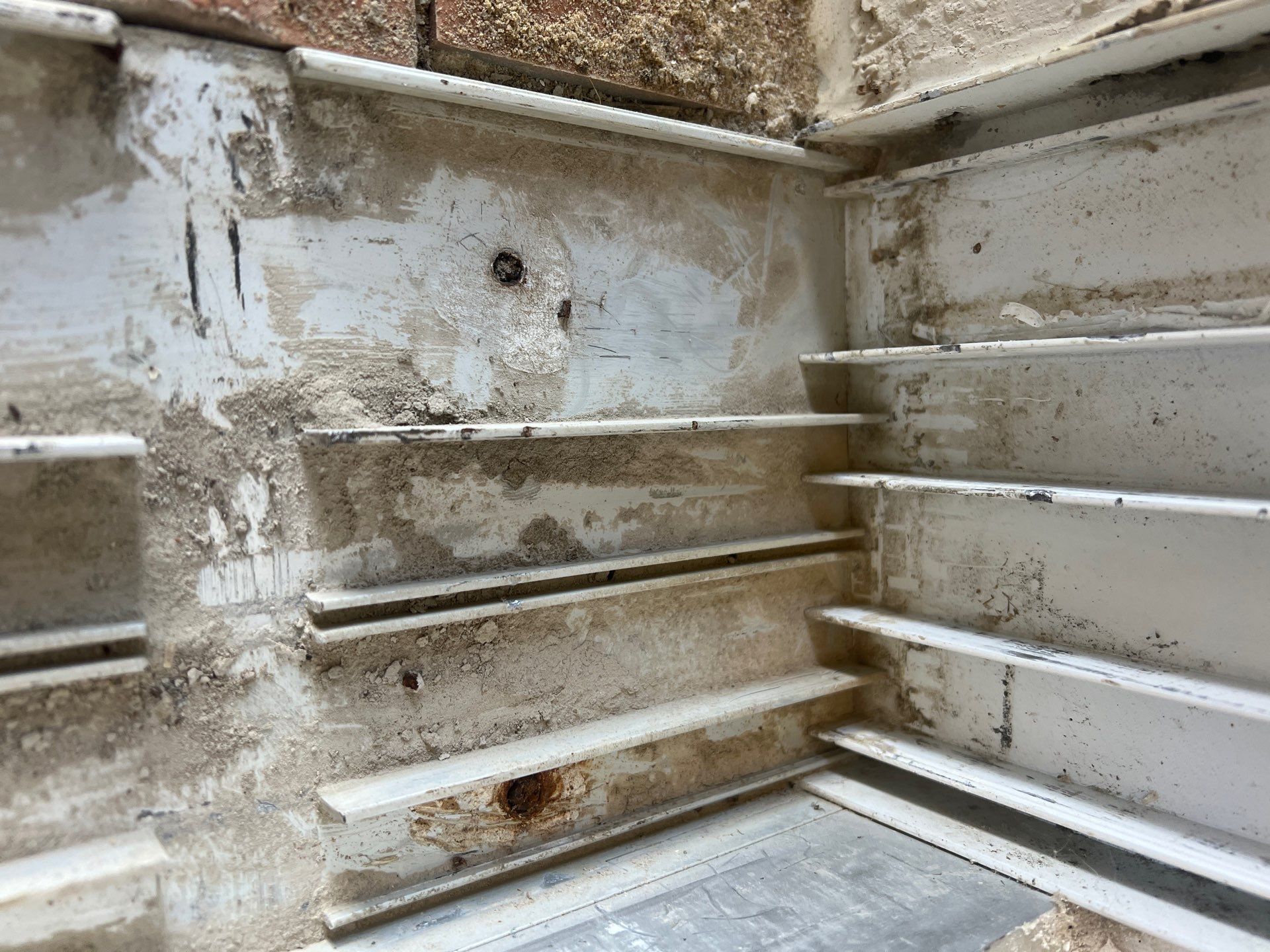 An interior view of a corner showing damaged, weathered white walls with horizontal metal structural supports.