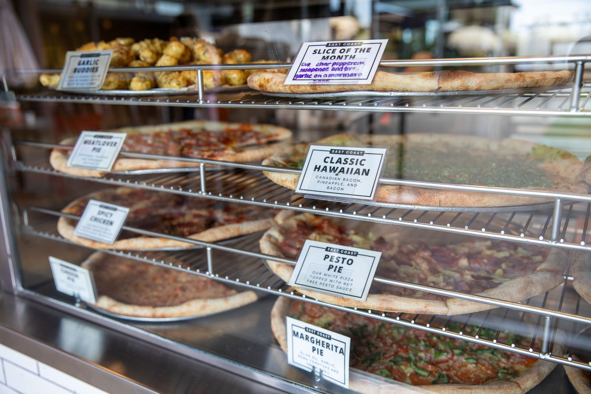 A display case filled with a variety of East Coast Pizza pizzas and pastries.