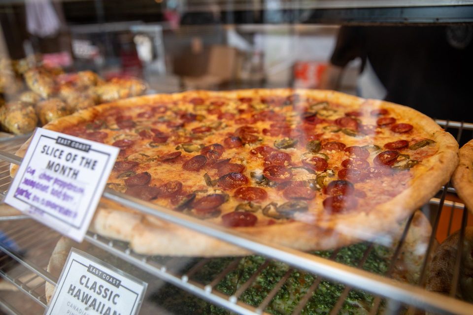 Pizza slice of the month in a display case, with pepperoni and green peppers.