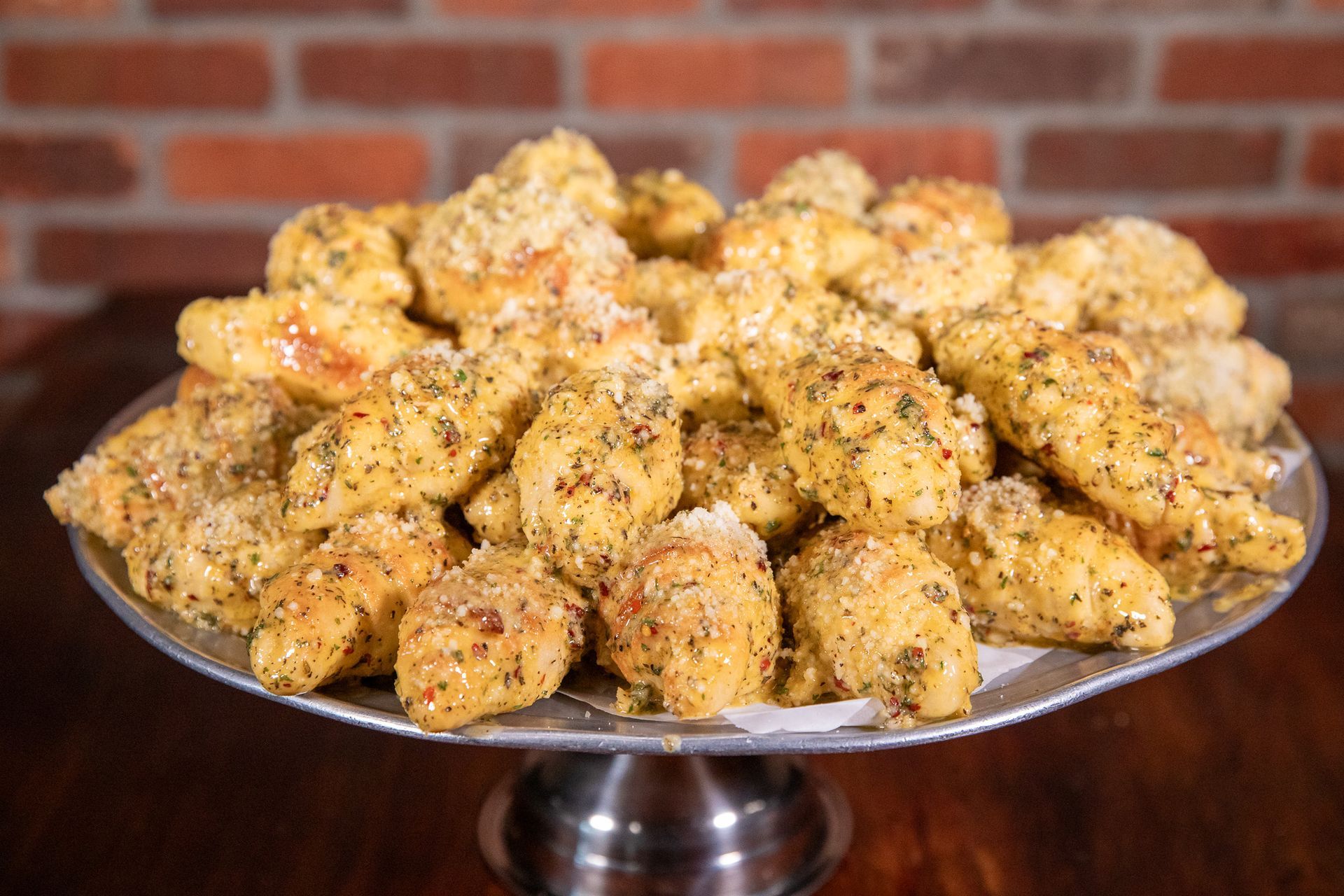 A silver platter piled high with golden, seasoned chicken wings against a brick wall.