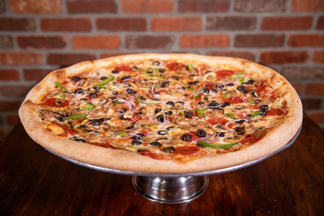 Pizza with various toppings on a silver stand in front of a brick wall.
