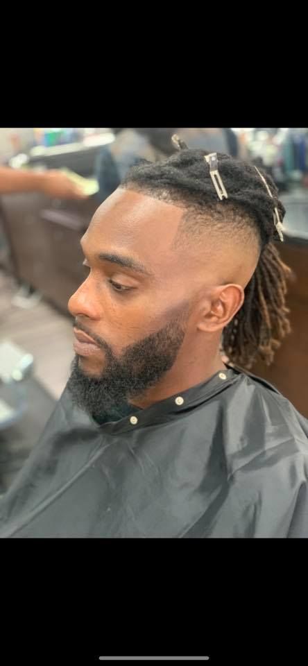 A man with dreadlocks and a beard is getting his hair cut at a barber shop.