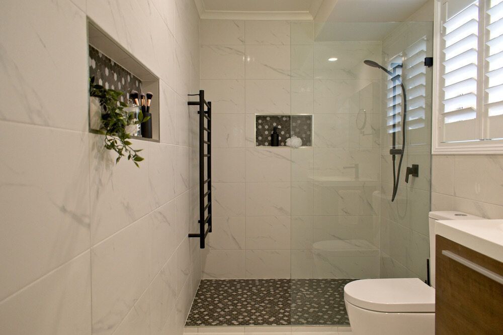 Modern Bathroom With Marble Walls, Glass Shower, Black Towel Rack, and Pebble Floor — Datco Windows & Doors Pty Ltd In South Murwillumbah, NSW