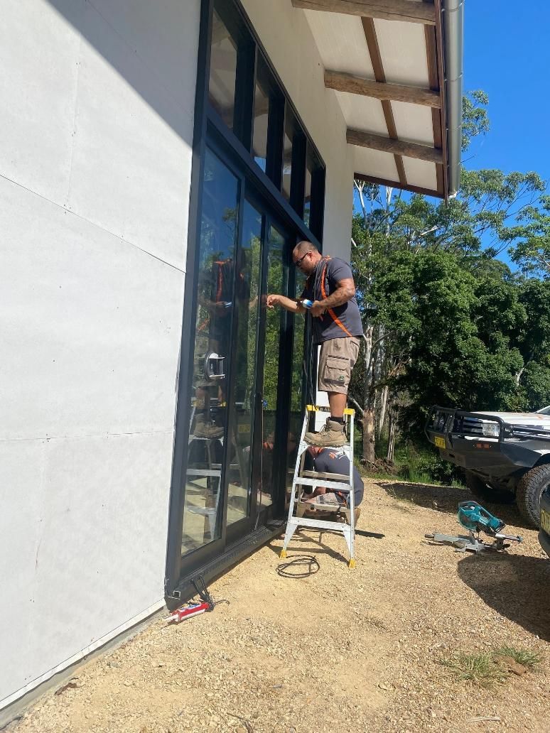 A Man Is Standing On A Ladder In Front Of A Building — Datco Windows & Doors Pty Ltd In Tweed Coast, NSW