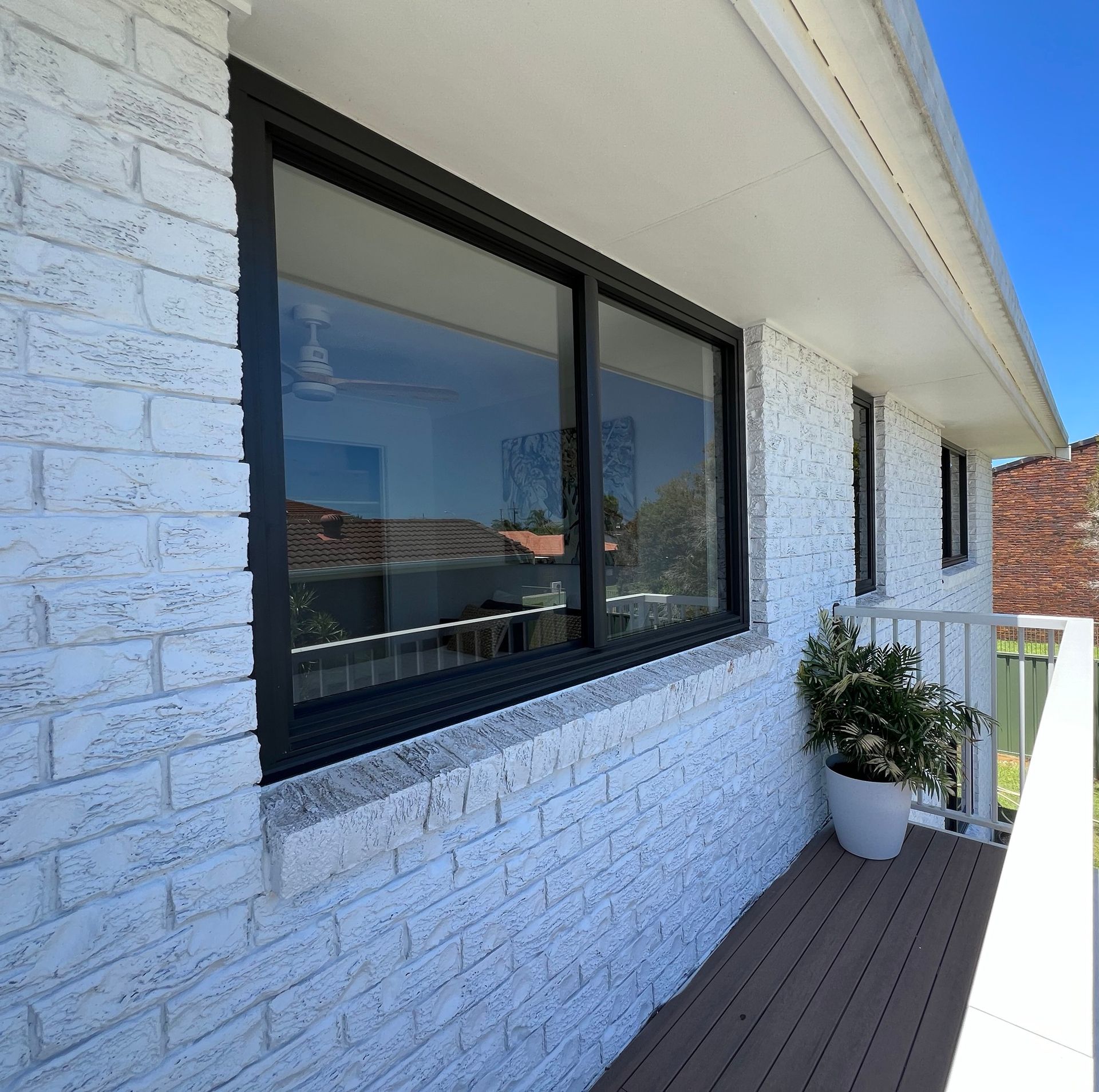 Exterior View of a House With White Brick Walls, Black-framed Window, and Wooden Deck — Datco Windows & Doors Pty Ltd In South Murwillumbah, NSW