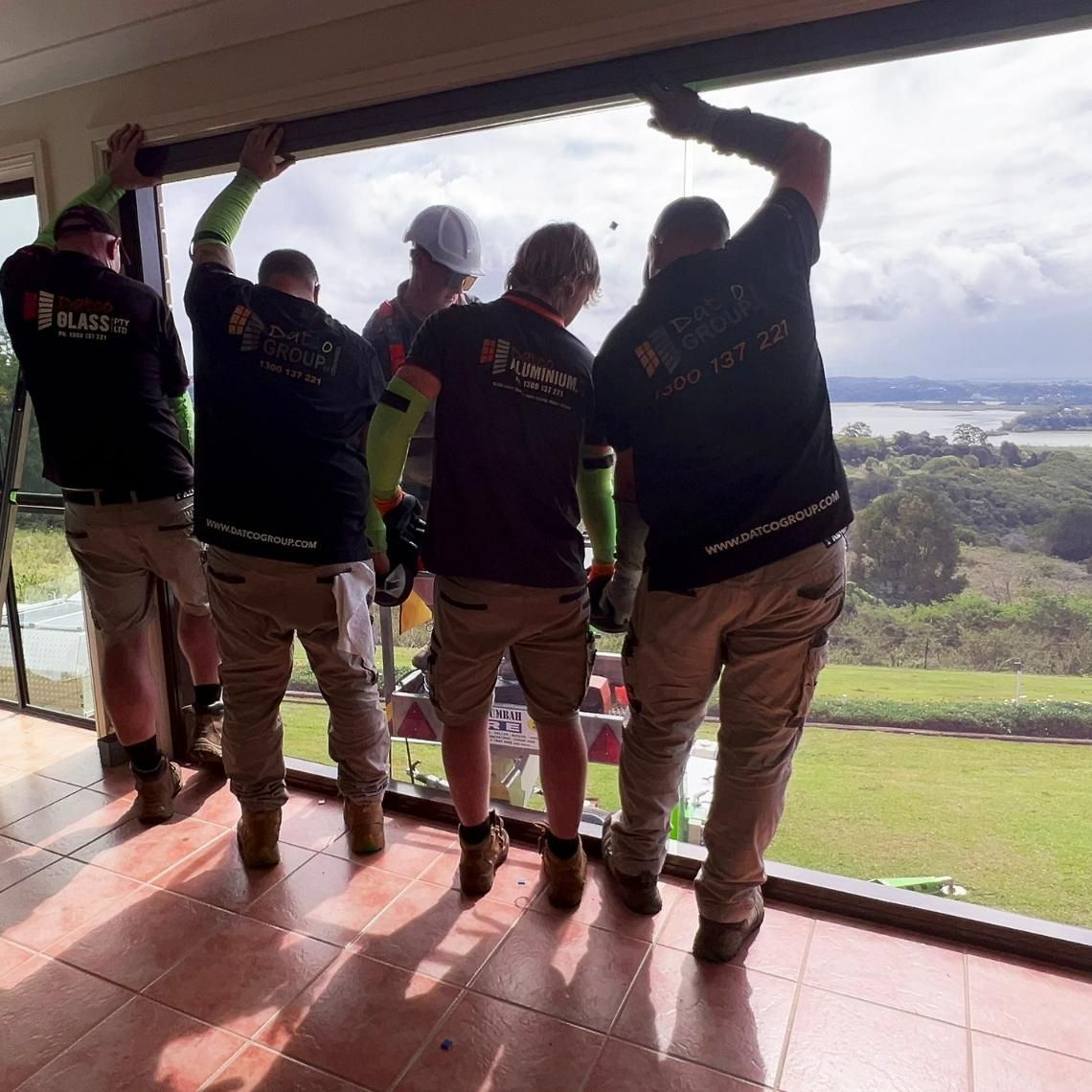 A Group Of Men Are Standing On A Balcony Looking Out A Window — Datco Windows & Doors Pty Ltd In South Murwillumbah, NSW