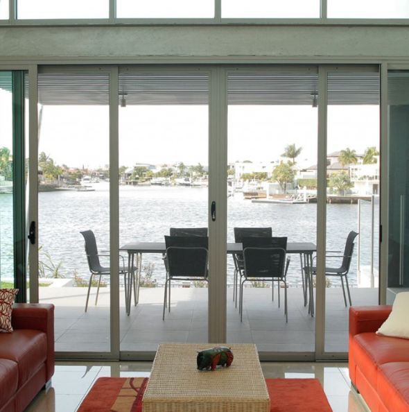 Modern living room with sliding glass doors to a waterfront patio and dining table — Datco Windows & Doors Pty Ltd In South Murwillumbah, NSW