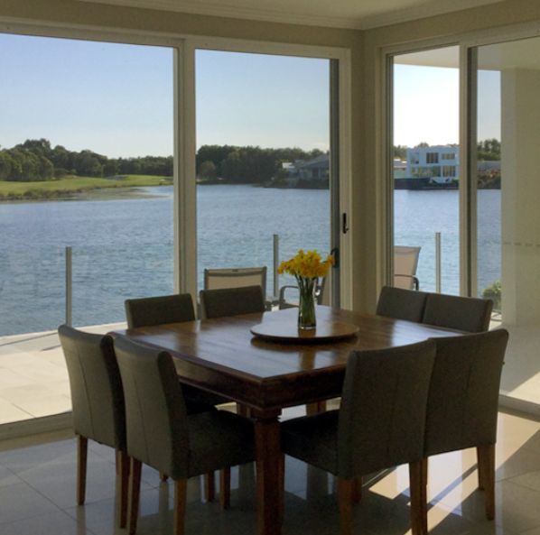 Dining table by large windows overlooking a calm waterfront — Datco Windows & Doors Pty Ltd In South Murwillumbah, NSW