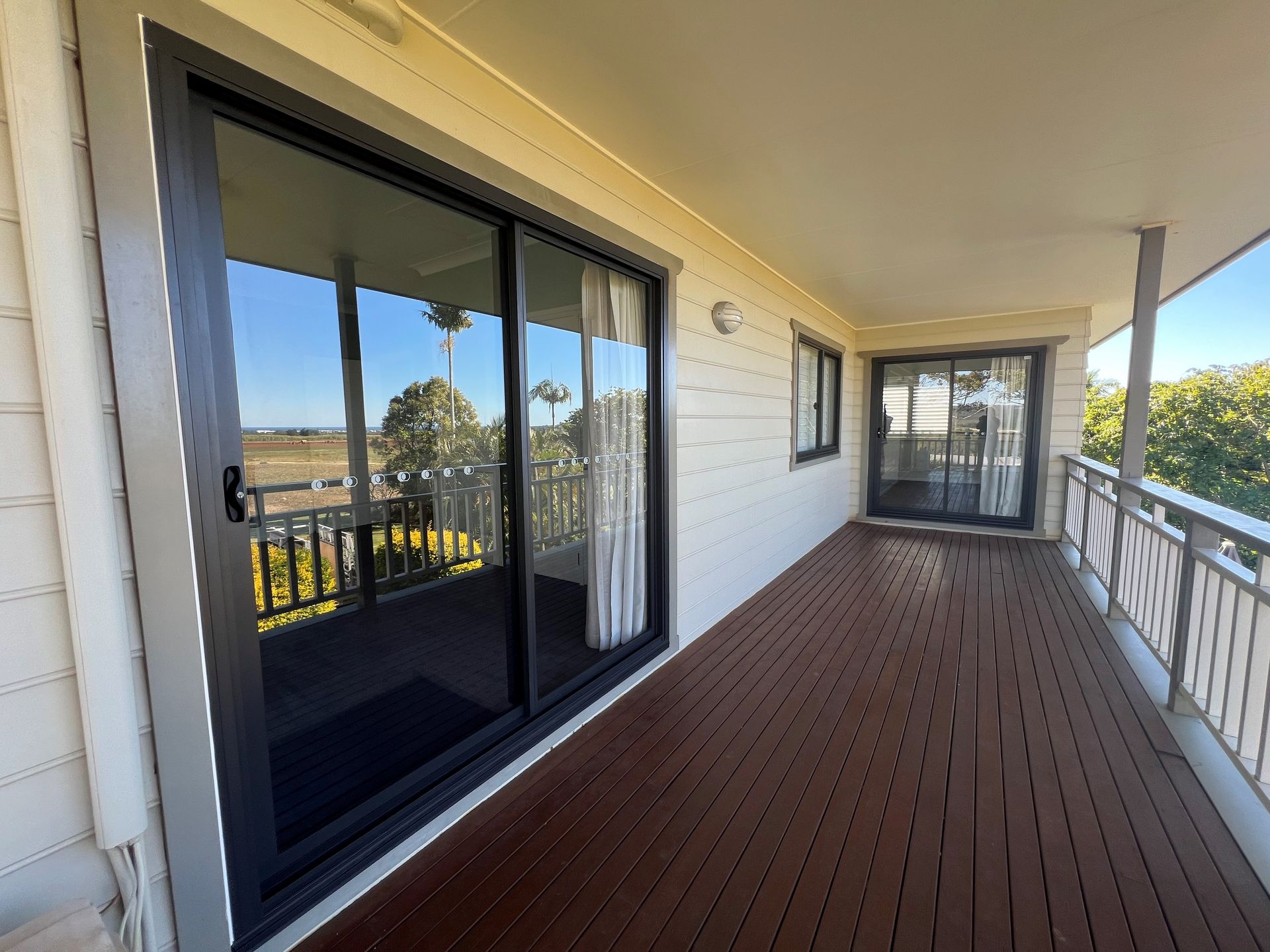 Covered porch with sliding glass doors, white railings, and a brown wooden floor — Datco Windows & Doors Pty Ltd In South Murwillumbah, NSW