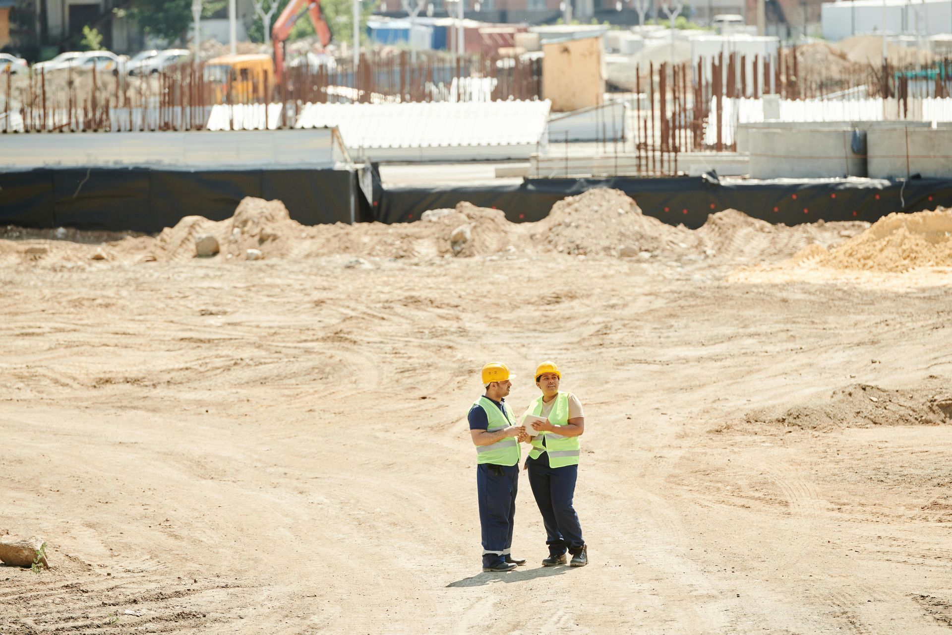 Two construction workers in yellow helmets and vests on a construction site.