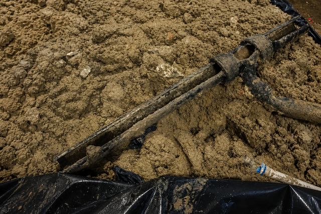 Shovel handle in a pile of tan sand beside black tarp and rope