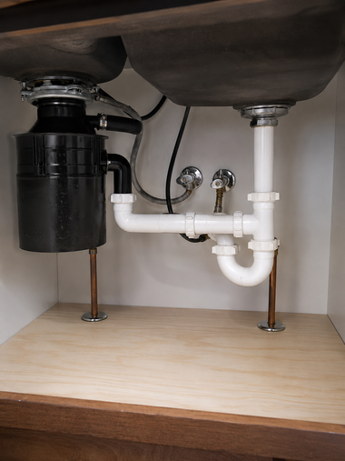 Under-sink plumbing with white pipes and a black garbage disposal beneath a bathroom sink