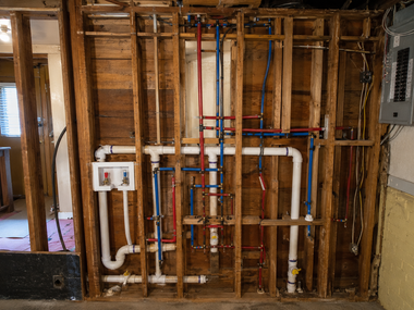 Exposed plumbing pipes and electrical wiring inside unfinished wall framing in a renovation site