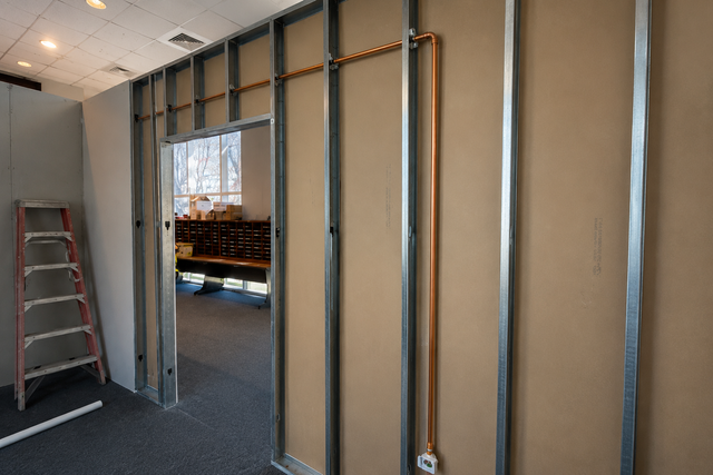 Partially framed interior wall in a room, with exposed studs and a red ladder nearby