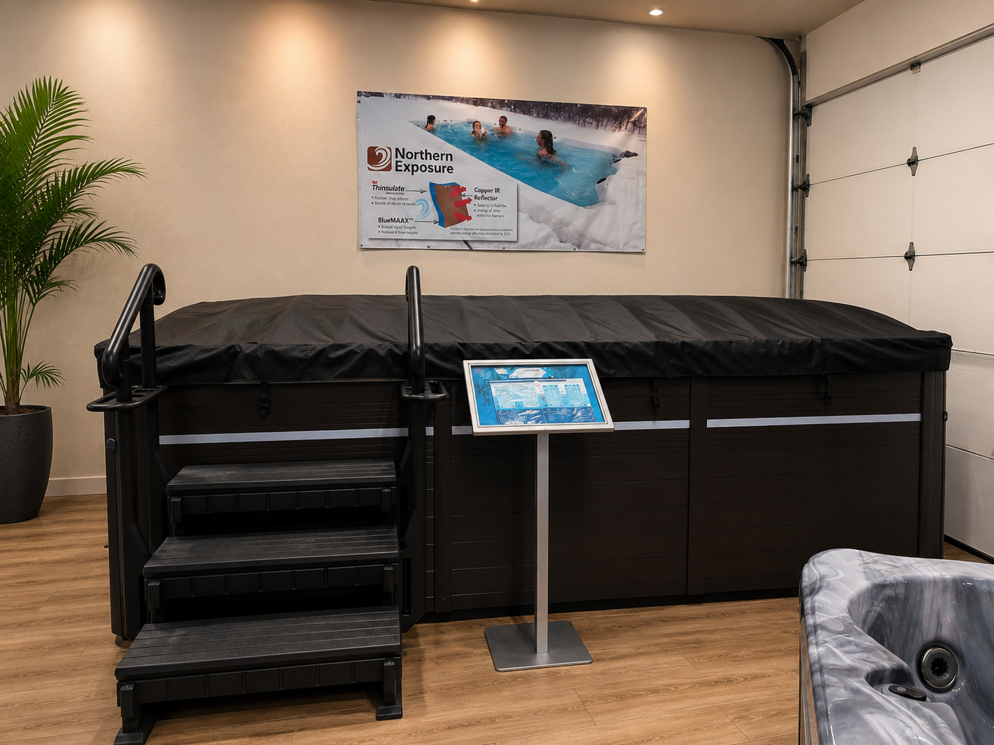 Indoor hot tub area with black spa, steps, sign, and wall poster
