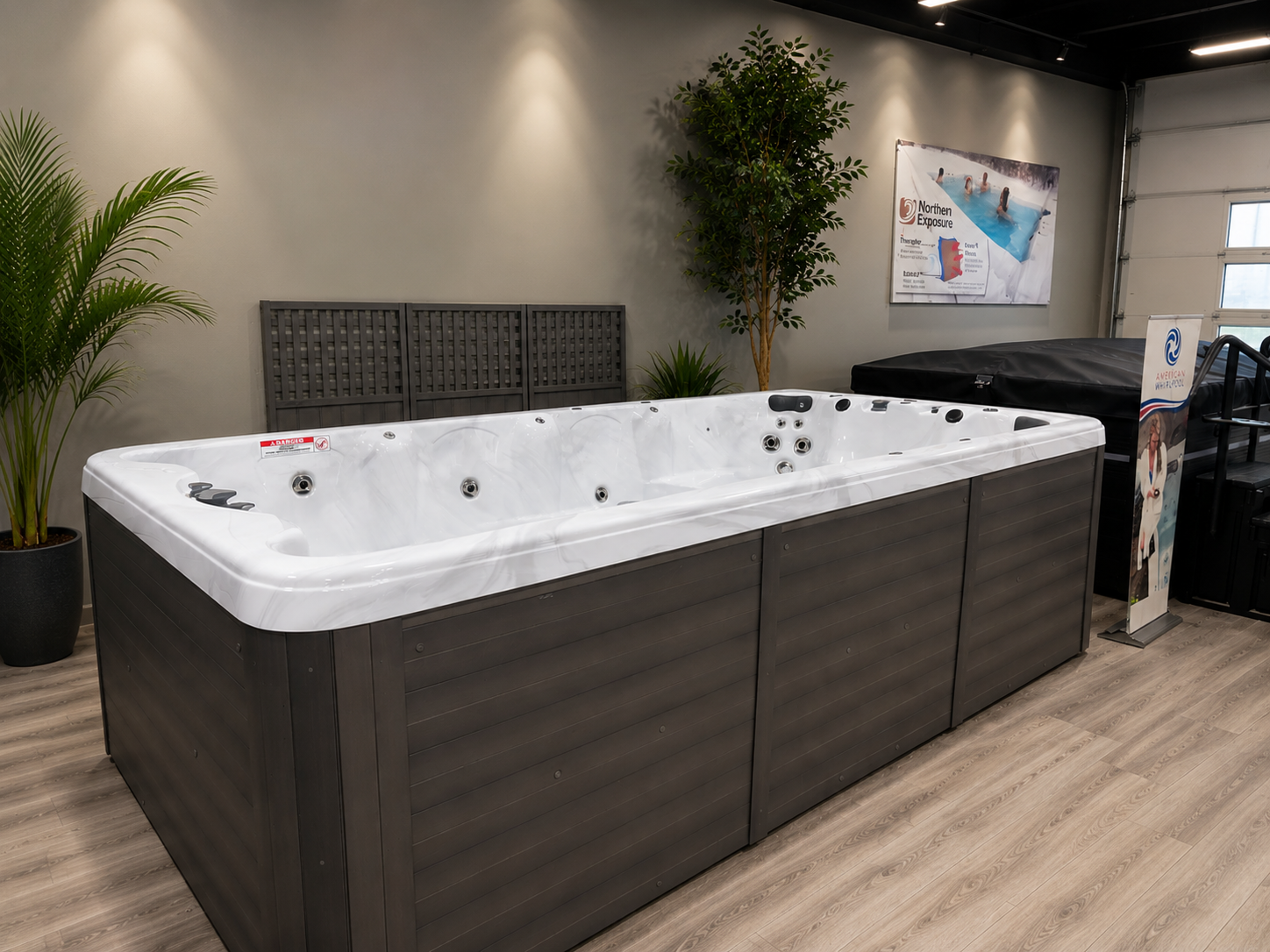Indoor showroom hot tub with dark gray exterior and white interior, surrounded by potted plants