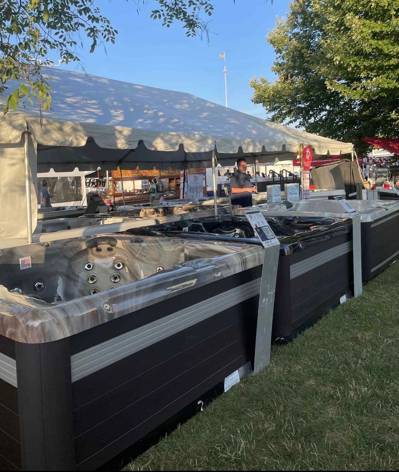 Outdoor hot tubs lined up beside a large white tent at an outdoor spa event