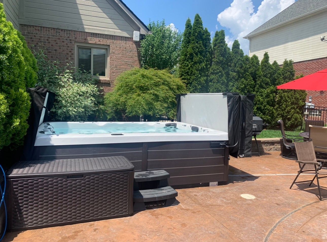 Backyard above-ground pool with hot tub, black deck, and patio furniture on a sunny day
