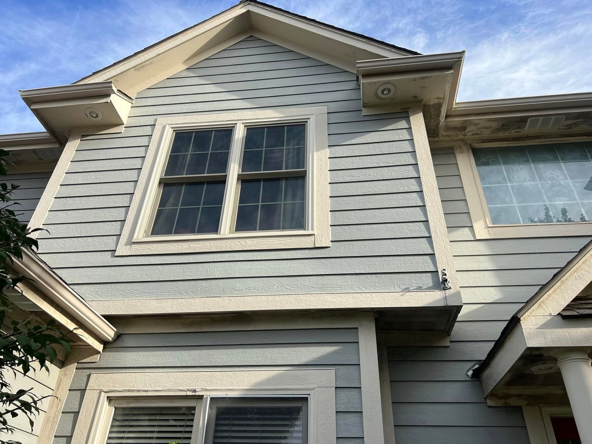 Blue siding on a two-story building with white trim and windows under a partly cloudy sky.