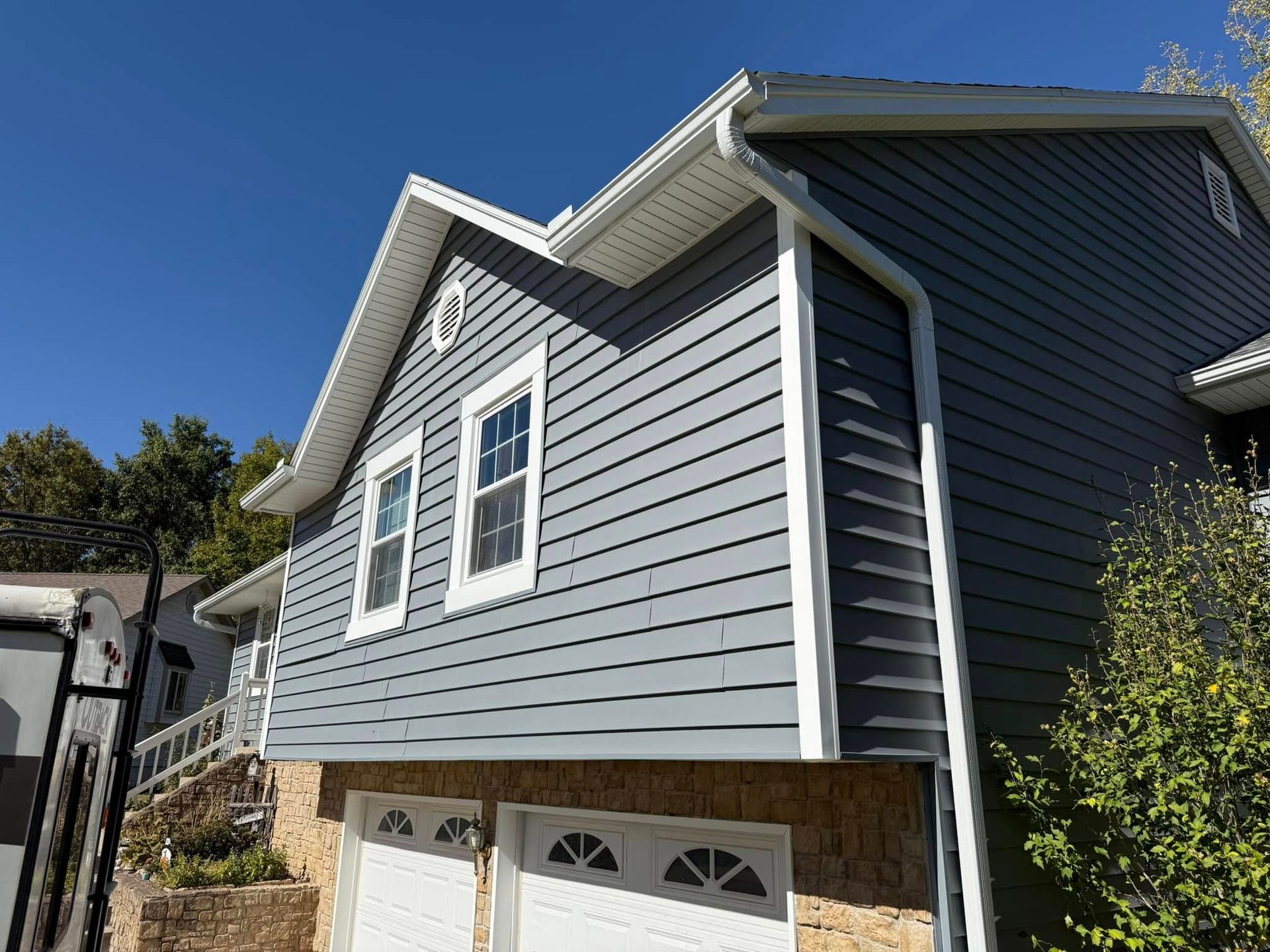 Two-story house with gray siding, white trim, and two garage doors; blue sky in background.