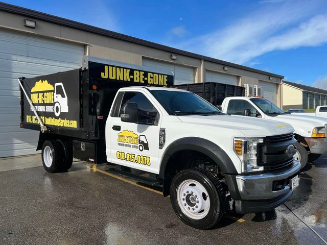White Junk-Be-Gone truck parked in front of buildings on a bright day. Truck bed is black, and the company logo is visible.