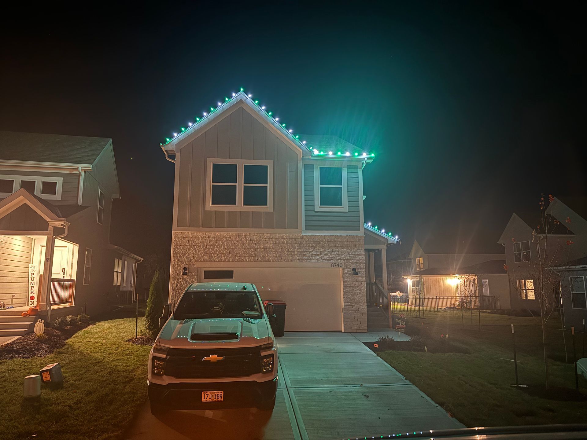 House at night with green and white lights on roof, truck in driveway.