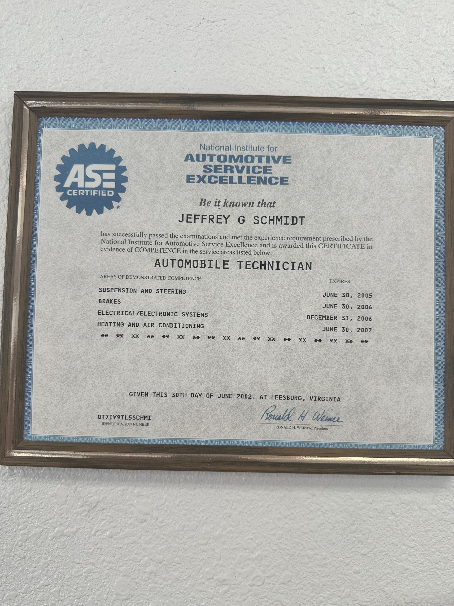 Framed Automotive Service Excellence certificate on a wall, with blue border and ASE logo.